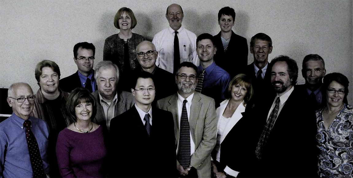 A group of 17 faculty members smiling posed for a yearbook photo